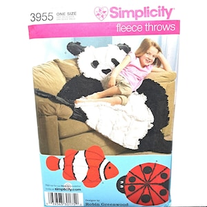 May include: Simplicity fleece throws pattern featuring a panda bear, clownfish, and ladybug designs. The pattern includes the number 3955 and the words "ONE SIZE". The image shows a child sitting on a panda bear throw.