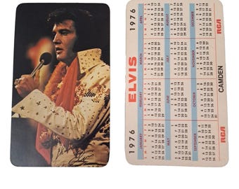 Puede incluir: Una tarjeta calendario rectangular de 1976 de Elvis Presley que muestra un retrato de Elvis con un mono blanco adornado y una bufanda roja sosteniendo un micrófono, y en el reverso, el calendario mensual completo de 1976 con texto RCA y Camden.