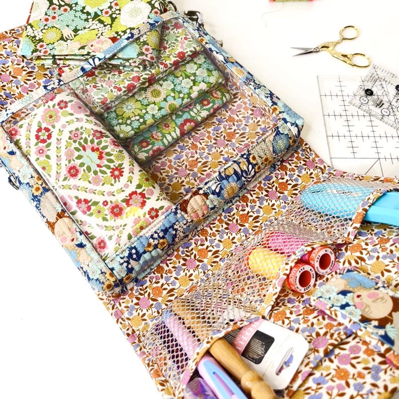 May include: A floral patterned fabric sewing kit with a clear plastic window to view the contents. The kit has multiple pockets and compartments for storing sewing supplies, including thread spools, needles, and other tools.