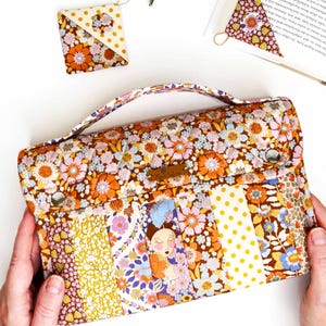 Pode incluir: Uma clutch com padr&atilde;o floral e al&ccedil;a, com um design de patchwork com flores laranja, amarelas e azuis. Um acess&oacute;rio quadrado e triangular a condizer tamb&eacute;m &eacute; vis&iacute;vel. A clutch tem uma etiqueta de couro castanho.