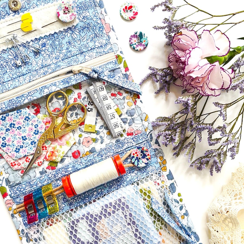 May include: A blue and white fabric zippered pouch with a variety of sewing supplies, including scissors, thread, and a measuring tape. The pouch is open and the supplies are visible. There are also some decorative buttons and flowers on the pouch.