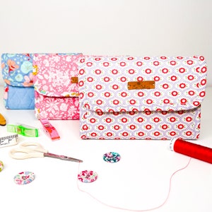 May include: Three fabric zippered pouches with floral patterns. The pouches are lined up in a row on a white surface. The pouch on the right has a brown label with the text "Mer' Couture".