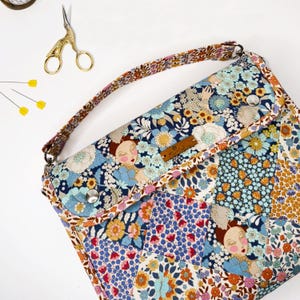 May include: A floral patterned fabric bag with a long strap. The bag has a flap closure with a button and a small leather label that says "The Maker's Atelier".