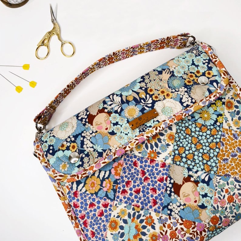 May include: A floral patterned fabric bag with a long strap. The bag has a flap closure with a button and a small leather label that says "The Maker's Atelier".