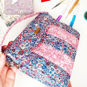 May include: A blue and pink floral fabric bag with a flap closure and a strap. The bag has a quilted design and is decorated with white buttons.