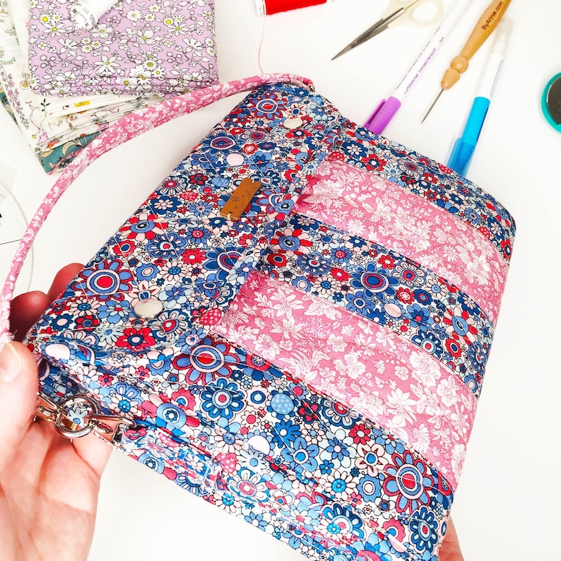 May include: A blue and pink floral fabric bag with a flap closure and a strap. The bag has a quilted design and is decorated with white buttons.