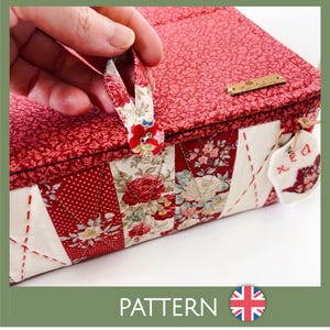 Puede incluir: Una caja de tela roja y con estampado floral con cierre de botón y una pequeña etiqueta. La caja presenta un diseño de patchwork con telas rojas y blancas. La palabra "PATTERN" se muestra en la parte inferior de la imagen.