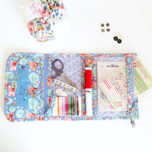 May include: A blue fabric sewing kit with multiple compartments. The kit is open and contains a pair of scissors, a small ruler, a spool of red thread, a spool of white thread, a pack of assorted needles, and a small pack of buttons. The kit is labelled "Buttons".