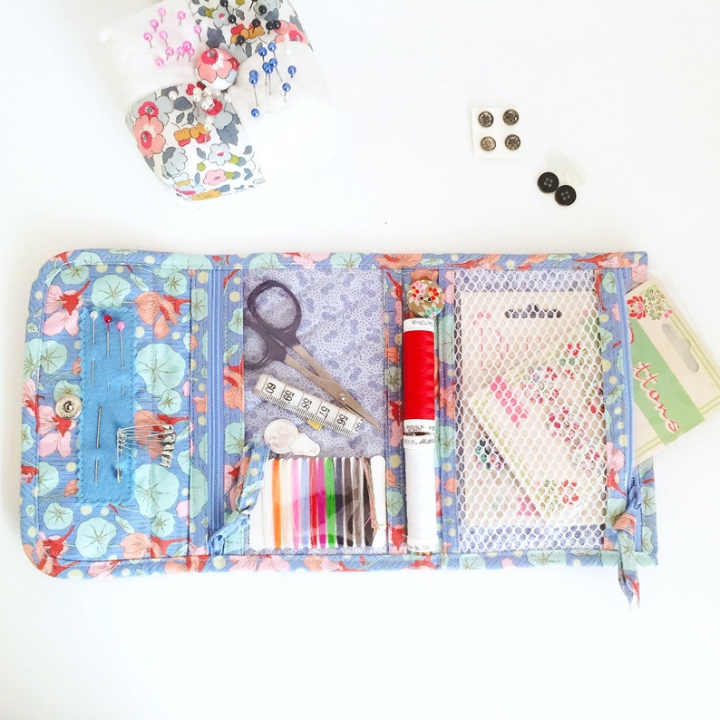 May include: A blue fabric sewing kit with multiple compartments. The kit is open and contains a pair of scissors, a small ruler, a spool of red thread, a spool of white thread, a pack of assorted needles, and a small pack of buttons. The kit is labelled "Buttons".