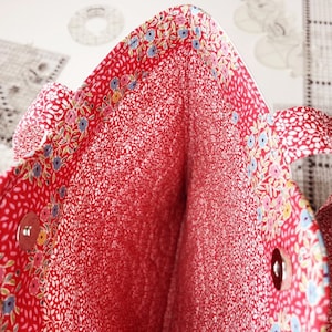 Puede incluir: El interior de una bolsa de mano roja con estampado floral. La bolsa tiene dos asas y un cierre de presi&oacute;n.