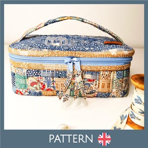 Może przedstawiać: Pikowana, prostokątna kosmetyczka z niebieskim zamkiem błyskawicznym i uchwytem. Torba ma wzór patchworkowy z różnymi wzorami, w tym domami i motywami kwiatowymi. Na dole napis "PATTERN".