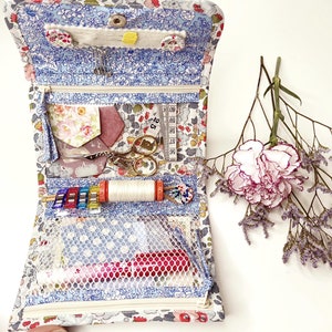May include: A blue and white floral fabric zippered pouch with a mesh pocket. The pouch is open and filled with sewing supplies, including thread, needles, scissors, and a measuring tape.