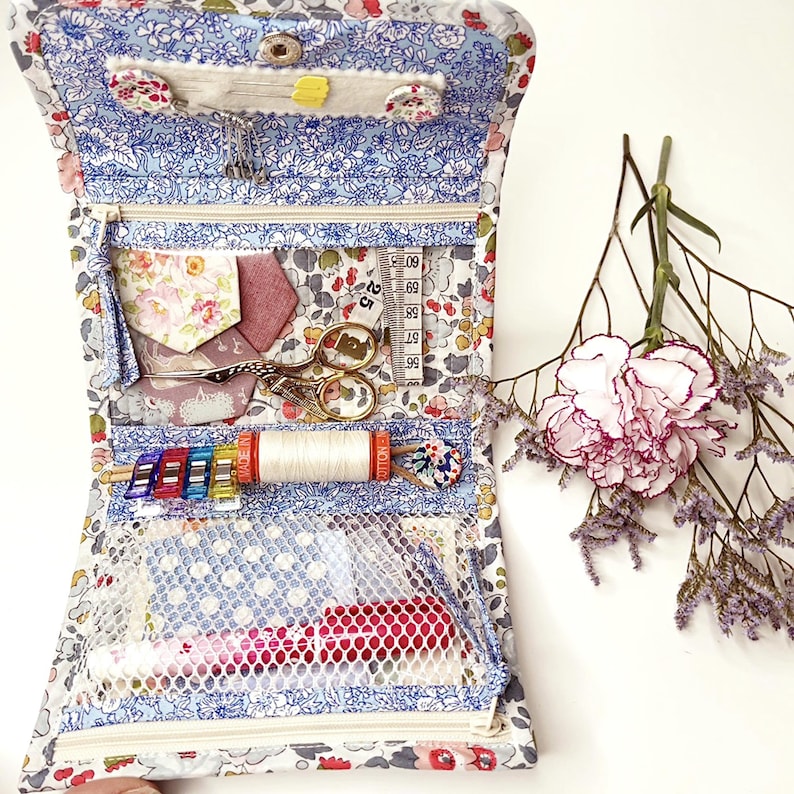 May include: A blue and white floral fabric zippered pouch with a mesh pocket. The pouch is open and filled with sewing supplies, including thread, needles, scissors, and a measuring tape.
