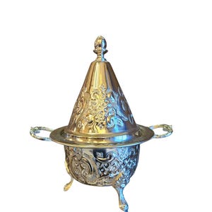May include: A silver-plated sugar bowl with an ornate design and a conical lid. The bowl has three legs and two handles.