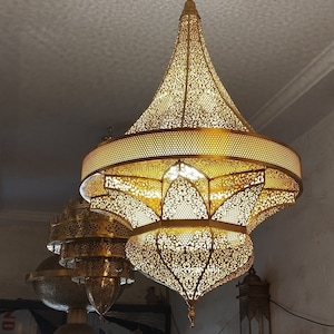 May include: A set of three ornate gold-colored metal chandeliers with intricate cut-out designs. The chandeliers are hanging from the ceiling and are illuminated with warm white lights.