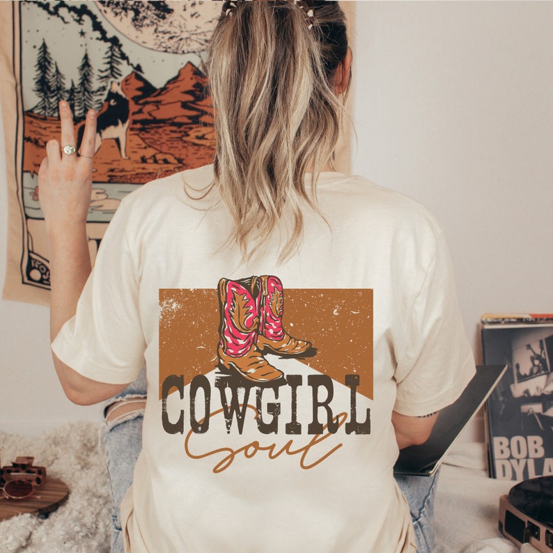 May include: A beige t-shirt with a brown and orange graphic of cowboy boots and the text "COWGIRL Soul" printed on the back.