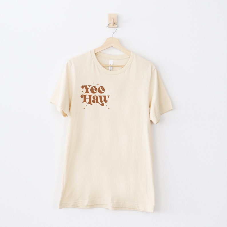 May include: A cream colored t-shirt with a brown graphic that says "Yee Haw" in a retro font.