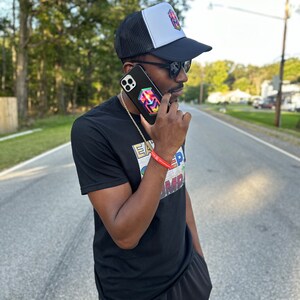 May include: Black trucker hat with a white front panel and a colorful geometric design. The person is wearing a black t-shirt with the text "EAT SLEEP..." and a matching phone case. The person is also wearing sunglasses and a gold chain.