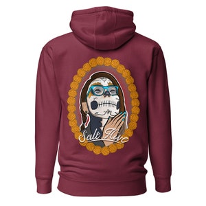 Può includere: Felpa con cappuccio bordeaux con un design del Giorno dei Morti. La grafica include il volto di una donna dipinto come un teschio di zucchero, con occhiali blu e incorniciato da un ovale floreale dorato. Il testo "Salt Hive" è sotto.
