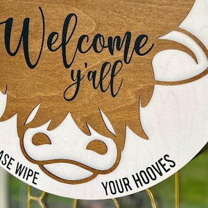 All season door hanger laser cut image long hair highland cow. Humorous "Please wipe your hooves"