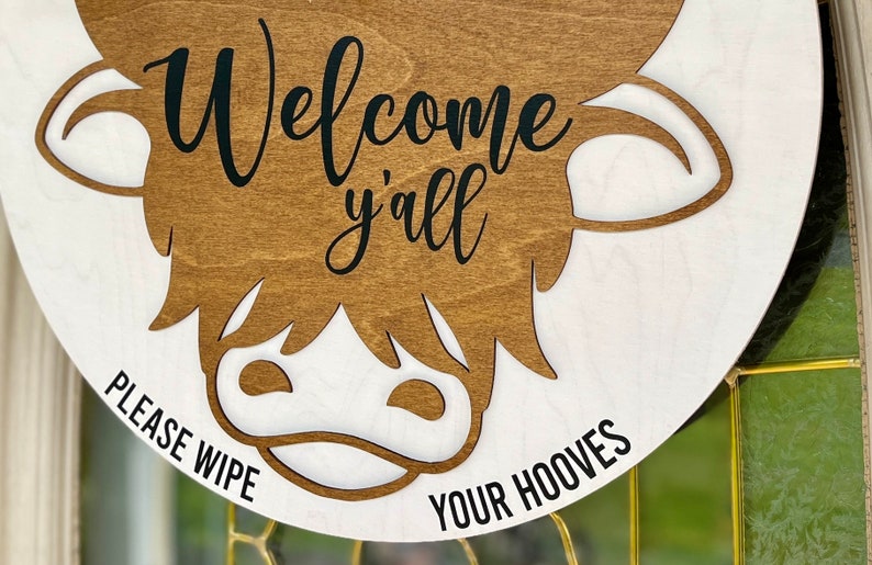 All season door hanger laser cut image long hair highland cow. Humorous "Please wipe your hooves"