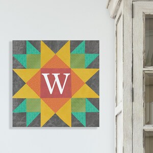 May include: A colorful quilt block with a star design in shades of yellow, orange, red, green, and gray. The center of the block features a white letter "W" on a red background.