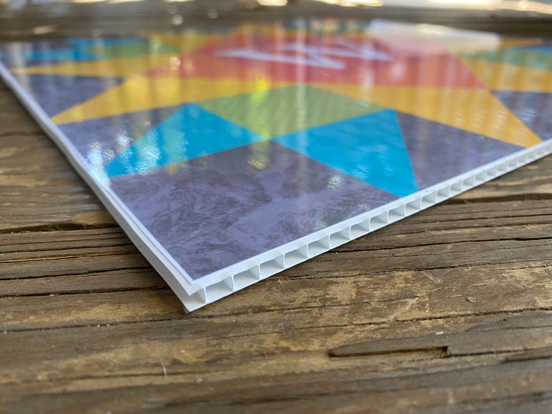 May include: Close-up of the edge of a colorful printed sign with a white corrugated plastic backing.