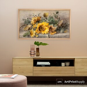 May include: A framed print featuring a still life of sunflowers in shades of yellow and brown, with green leaves. The artwork is displayed above a wooden cabinet. Two decorative vases and a plant are on the cabinet.