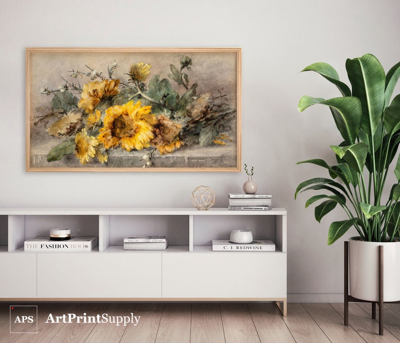 May include: A framed watercolor print featuring a still life of sunflowers in shades of yellow and brown. The artwork is displayed above a white cabinet with decorative items and a potted plant. The print is labeled "ArtPrintSupply" in the bottom left corner.