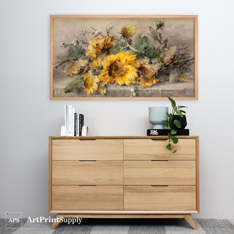May include: A framed watercolor print of sunflowers in shades of yellow and brown. The artwork is displayed above a light wood dresser with six drawers. The dresser has a mid-century modern design. The text "ArtPrintSupply" is in the bottom left corner.