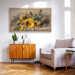 May include: A framed watercolor painting of sunflowers in shades of yellow, brown, and green. The artwork is displayed on a white wall above a wooden cabinet. The painting is in a light brown wooden frame.