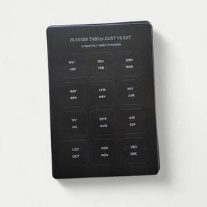 May include: Black planner tabs with white text for each month of the year. The text reads "Planner Tabs by Saint Violet" and "12 Monthly Index Stickers".