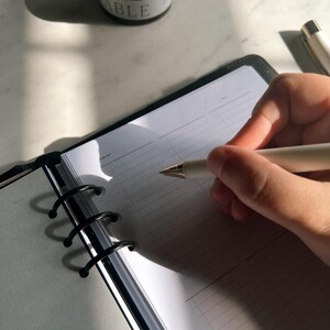 Puede incluir: Una agenda negra y blanca con un bol&iacute;grafo plateado y una vela negra con la palabra "ABLE" en ella. La agenda tiene un sistema de encuadernaci&oacute;n en espiral y est&aacute; abierta en una p&aacute;gina en blanco.