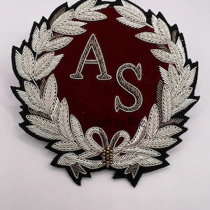 May include: A red velvet patch with a silver embroidered wreath and the letters "AS" in the center.