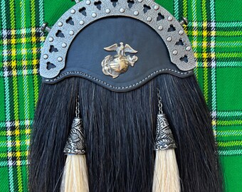 Puede incluir: Sporran de kilt de pelo de caballo negro y blanco con un emblema de águila, globo y ancla de plata. El sporran tiene dos borlas blancas con puntas de plata.