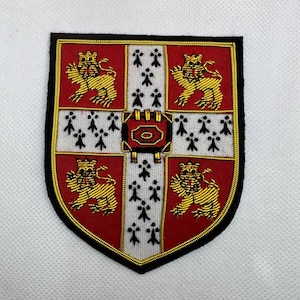 May include: Embroidered patch featuring a shield design with a red background and gold trim. The shield is divided into quadrants with gold lions and white stripes with black accents. A detailed emblem is at the center.