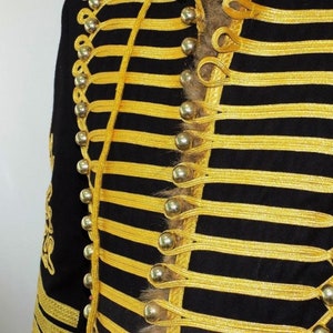 May include: A black jacket with gold trim and silver buttons. The jacket has a military style with a row of buttons down the front and a decorative braid.