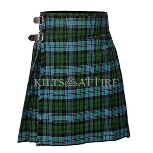 Puede incluir: Una falda escocesa con un patr&oacute;n de cuadros tart&aacute;n en verde, negro y azul claro. La prenda incluye dos correas de cuero negro con hebillas de metal plateado en el lateral para el cierre. El texto KILTS ATTIRE est&aacute; impreso en el centro.