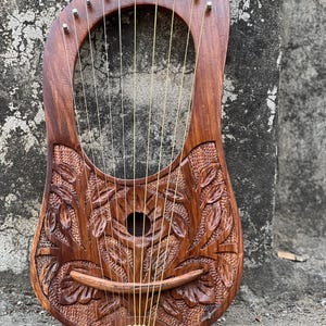 May include: A wooden lyre with a floral carving design. The lyre has 10 strings and is made of dark brown wood.