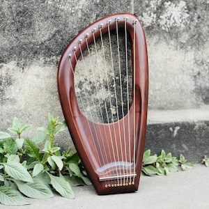 May include: A mahogany lyre with gold strings. The instrument has a curved, teardrop-shaped frame with tuning pegs at the top. The strings are stretched vertically, creating a musical instrument.