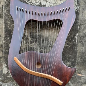 May include: A dark brown wooden lyre with a curved soundboard and a row of tuning pegs along the top. The lyre has a total of 20 strings and a wooden sound bar.