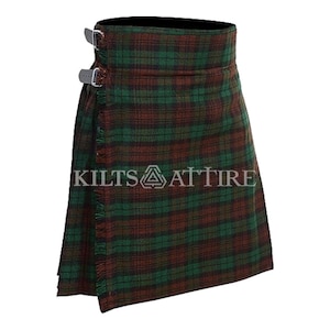 Puede incluir: Una falda escocesa con un patr&oacute;n de tart&aacute;n a cuadros verdes y marrones con un borde deshilachado en el panel frontal. La prenda incluye dos hebillas met&aacute;licas plateadas ajustables en el lateral y muestra el texto KILTS ATTIRE en el centro.
