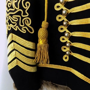 May include: A black jacket with gold trim and buttons. The jacket has a fur collar and a gold tassel on the sleeve.
