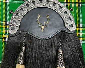Puede incluir: Sporran de kilt negro con un emblema de ciervo plateado y negro, dos borlas negras y blancas y un ribete de metal plateado y negro.