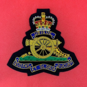May include: A black embroidered patch with a gold crown, cannon, and scroll. The scroll reads "Ubique Quo Fas Et Gloria Ducunt".