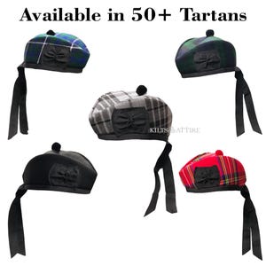 May include: Five tam o' shanter hats in various tartan patterns and solid black, each featuring a black pom-pom, a black bow detail, and two long black ribbons. The text "Available in 50+ Tartans" is displayed at the top of the image.