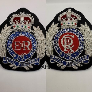 Op de afbeelding: Twee geborduurde patches met zilverdraad, met een kroon, een krans van bladeren en de woorden "HONI SOIT QUI MAL Y PENSE" en "ROYAL ENGINEERS". Het midden van elke patch is een rode cirkel met een zilveren "ER" of "R" erin.