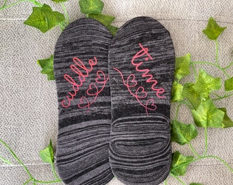 May include: A pair of black and grey socks with pink lettering. One sock says "cuddle time" and the other says "love time".
