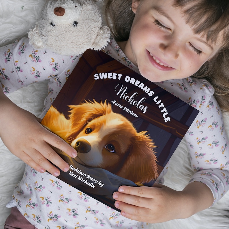 Puede incluir: Una ni&ntilde;a peque&ntilde;a sostiene un libro de cuentos para dormir titulado "Sweet Dreams Little Nicholas - Farm Edition." La portada del libro presenta un perro marr&oacute;n y blanco con el texto "Bedtime Story by Ersi Nicholls."