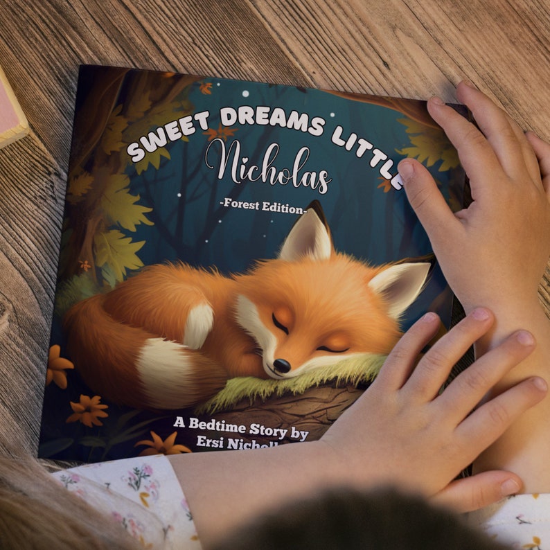 Może przedstawiać: Książka dla dzieci zatytułowana "Sweet Dreams Little Nicholas - Forest Edition" z ilustracją śpiącego pomarańczowego lisa. Książka jest otwarta, ukazując ilustrację na okładce. To bajka na dobranoc.